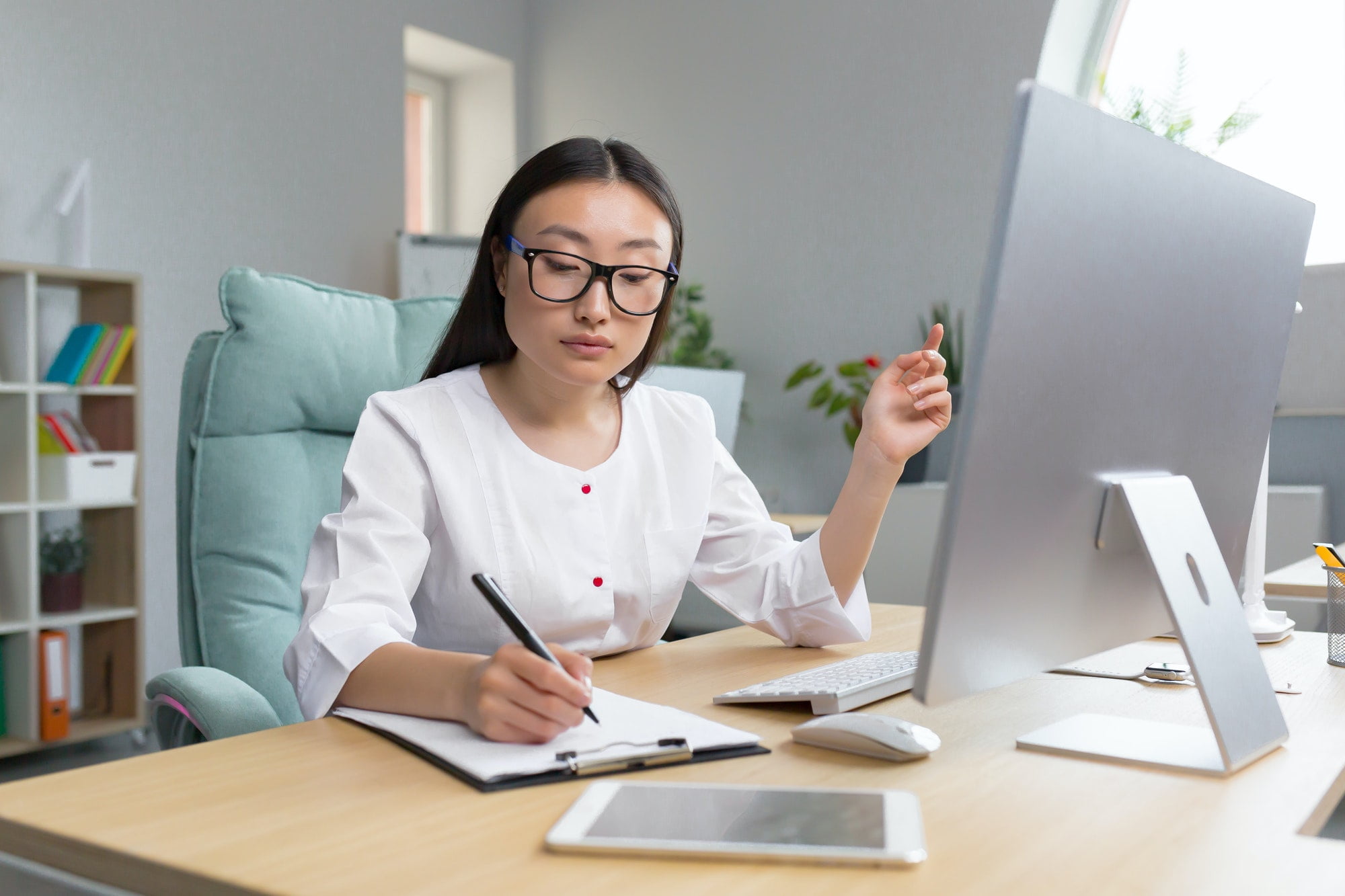 The work of a doctor. Young beautiful Asian woman doctor in glasses and medical gown in the office