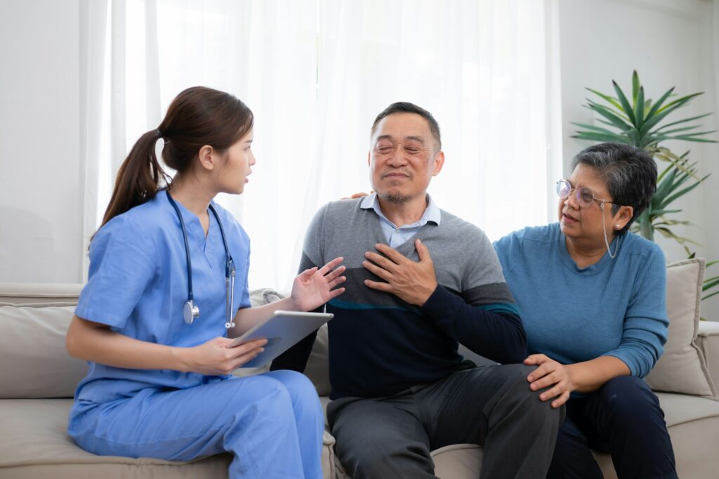 Asian senior patient talking with doctor and nurse on sofa at home