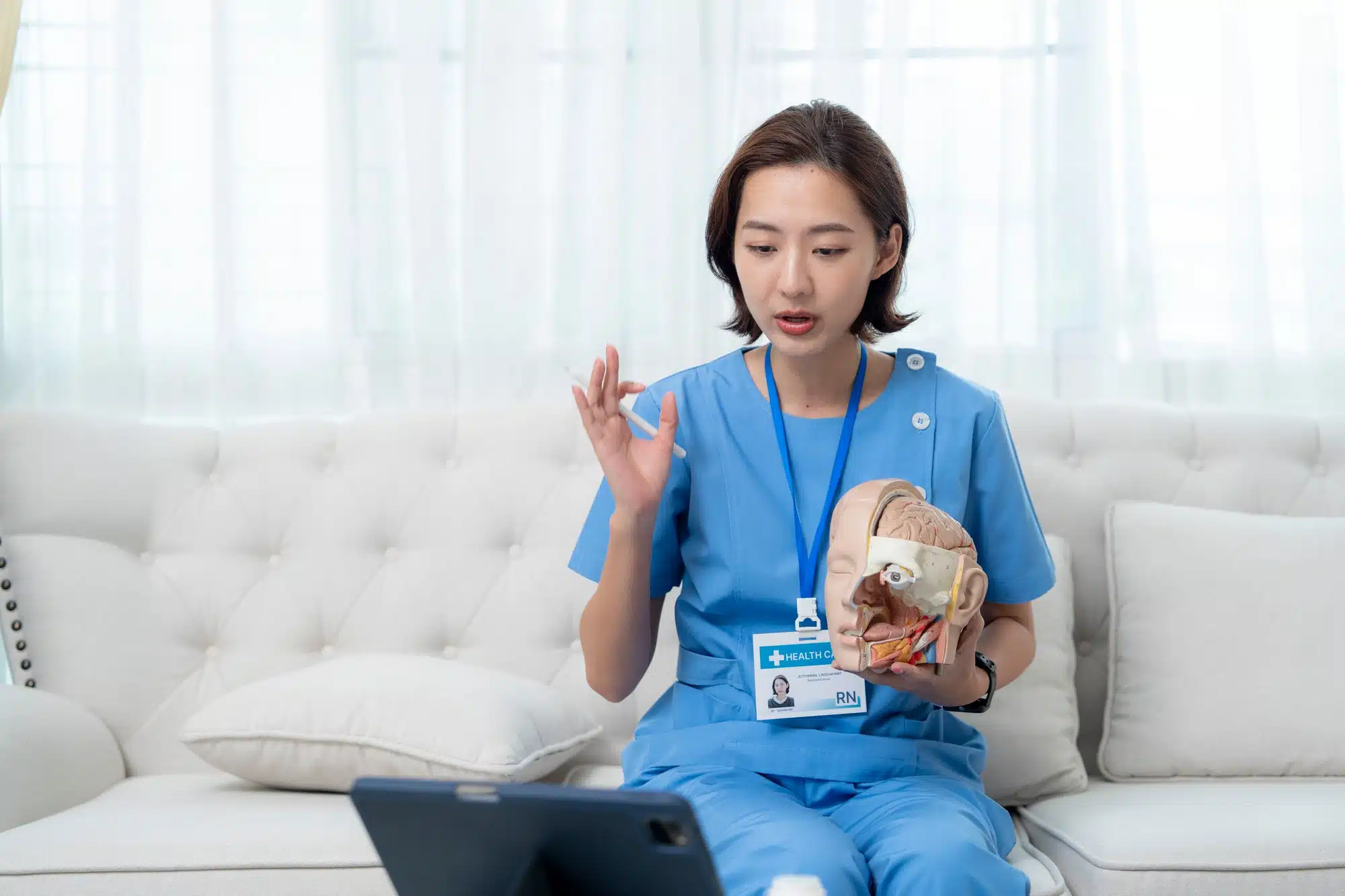 Healthcare professional in scrubs conducting a virtual consultation while holding a model of a human heart, emphasizing telemedicine.